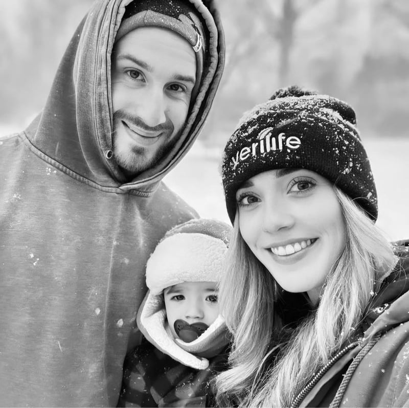 Amanda, her husband, and their little one standing together in the snow — a black and white family portrait